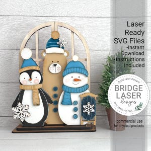 May include: A wooden winter decoration featuring a penguin, bear, and snowman. The penguin and snowman wear blue hats and scarves, while the bear has a blue hat. Each figure has a snowflake accent. The decoration is on a wooden base.