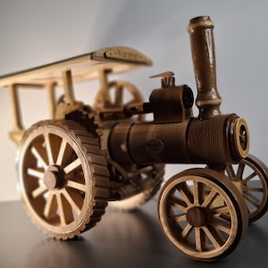 Puede incluir: Maqueta de madera detallada de un tractor de vapor antiguo. El juguete presenta grandes ruedas de madera, una chimenea y un dosel. El modelo está hecho de madera marrón clara y oscura, mostrando detalles intrincados.