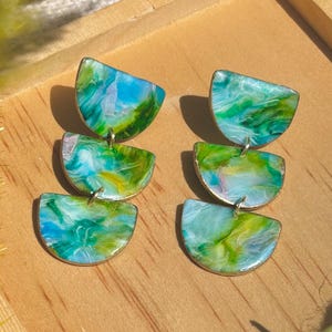 May include: A pair of green, blue, and white abstract swirl patterned earrings. Each earring is made of three stacked half-circle shapes.