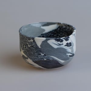 May include: A ceramic bowl with a unique marbled design in shades of gray, white, and black. The bowl's exterior features a blend of abstract patterns, creating a visually interesting texture. The interior is a solid gray color.