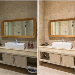 May include: A bathroom vanity with a white porcelain sink, a wooden framed mirror, and two bottles of liquid soap. The vanity has two cabinets with silver handles. The walls are tiled in a light beige color.