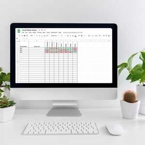 Op de afbeelding: Een computerscherm waarop een spreadsheet te zien is met de titel "Social Media Tracker" met kolommen voor verschillende sociale mediaplatforms en data. De spreadsheet is geopend in Google Sheets. De computer staat op een wit bureau met een toetsenbord en een muis. Er staan drie planten in potten op het bureau.
