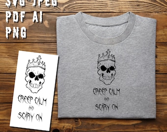 Può includere: Una maglietta grigia con un'illustrazione in bianco e nero di uno scheletro con una corona. Il testo "Creep Calm and Scary On" è stampato sotto lo scheletro.