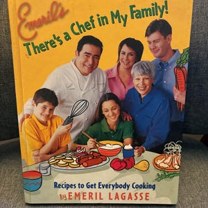 May include: A cookbook titled "Emeril's There's a Chef in My Family!" features a family portrait and food illustrations. The cover is yellow with text and images of people and food. The book's subtitle is "Recipes to Get Everybody Cooking" by Emeril Lagasse.