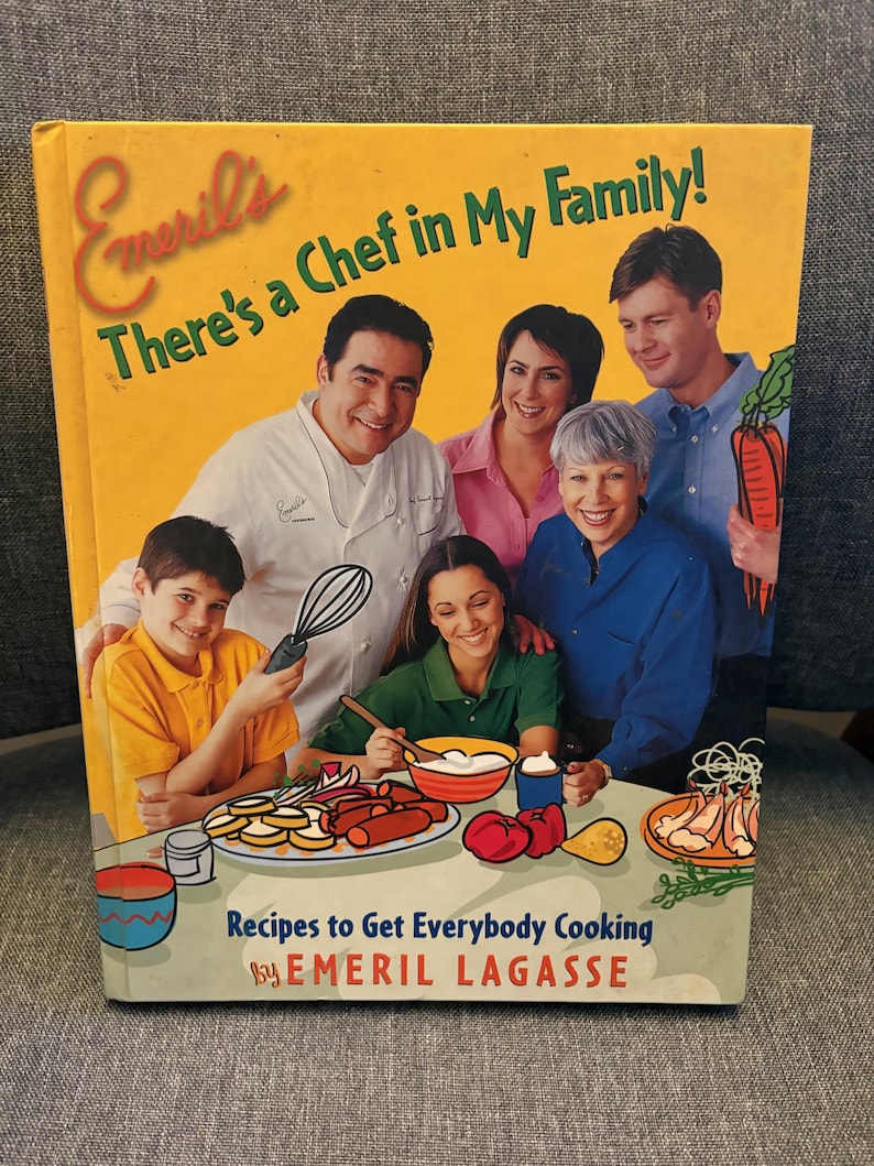 May include: A cookbook titled "Emeril's There's a Chef in My Family!" features a family portrait and food illustrations. The cover is yellow with text and images of people and food. The book's subtitle is "Recipes to Get Everybody Cooking" by Emeril Lagasse.