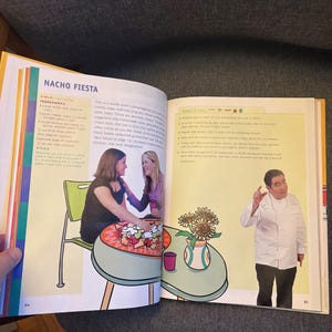May include: A cookbook open at a double-page spread, with the title "NACHO FIESTA." The left page has an illustration of a table with food and two women. The right page shows a chef gesturing near a table with sunflowers.