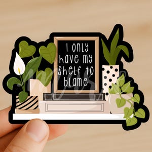 May include: A sticker featuring a shelf with potted plants and a framed sign. The sign reads "I only have my shelf to blame" in white script. The plants include a white flower, leafy green plants, and a plant in a black and white polka dot pot.