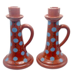 Può includere: Un paio di portacandele in terracotta con pois blu e un manico. I portacandele sono dipinti a mano e hanno un aspetto rustico.