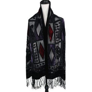 May include: A black sheer scarf featuring a geometric pattern of red and purple velvet diamond shapes and embroidered accents. The scarf has a solid black velvet border and a fringe trim along the bottom edge, displayed on a mannequin torso.