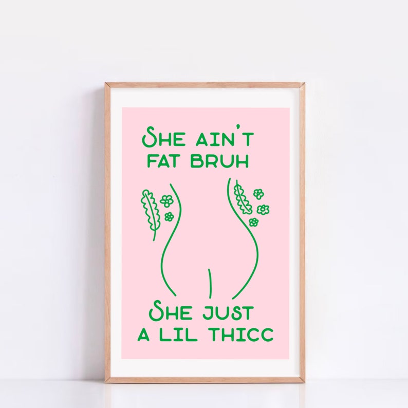 May include: A framed print with a pink background and green text. The text reads 'She ain't fat bruh she just a lil thicc.' The print features a simple line drawing of a woman's body with flowers on either side.