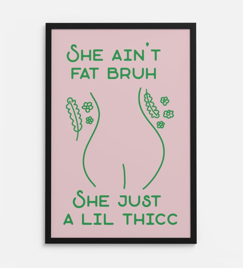May include: A framed poster with a pink background and green text. The text reads 'She ain't fat bruh she just a lil thicc.' The poster features a line drawing of a woman's body with flowers and leaves on either side.