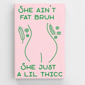 May include: A pink canvas print with green text and a line drawing of a body. The text reads 'She ain't fat bruh she just a lil thicc'.
