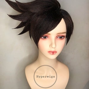 May include: A brown short wig with a side part and a few long strands of hair sticking up on one side. The wig is on a mannequin head with a white neck and chest. The text "Hyperwigs" is printed on the mannequin's chest.