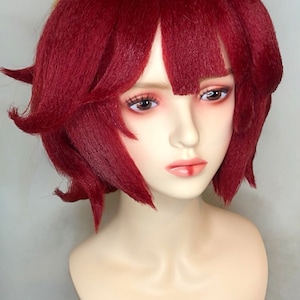May include: A red wig with a yellow topknot. The wig is styled in a short bob with bangs. The wig is on a mannequin head.