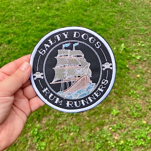 May include: A black and white embroidered patch with a white ship and the text "Salty Dogs Rum Runners" in a white circle.