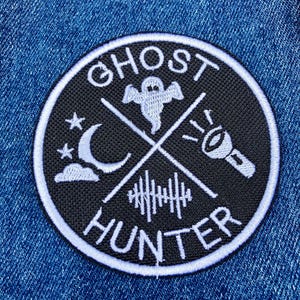 K&ouml;nnte beinhalten: Ein gestickter Patch in Schwarz und Wei&szlig; mit dem Text "Ghost Hunter" in einem Kreis. Der Patch zeigt ein Gespenst, einen Halbmond, eine Taschenlampe und einen Zaun.