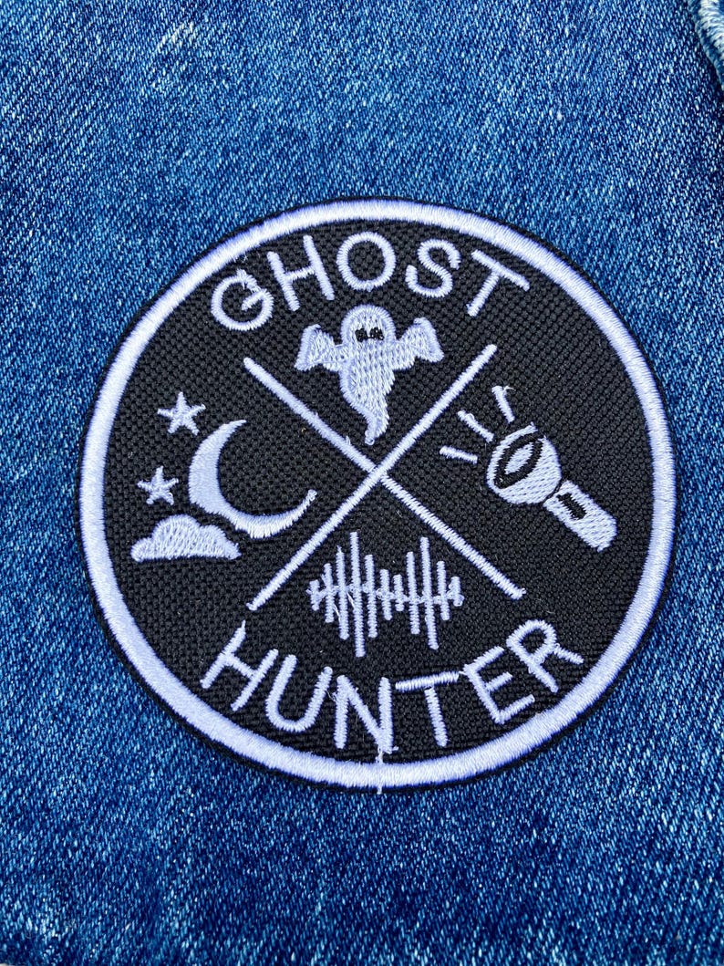 K&ouml;nnte beinhalten: Ein gestickter Patch in Schwarz und Wei&szlig; mit dem Text "Ghost Hunter" in einem Kreis. Der Patch zeigt ein Gespenst, einen Halbmond, eine Taschenlampe und einen Zaun.