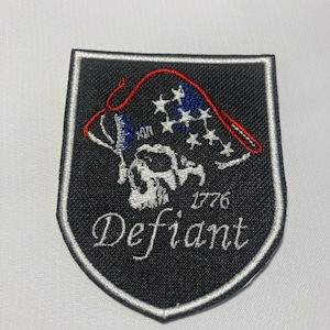 May include: Black embroidered patch with a white skull and a red, white, and blue American flag. The text "1776 Defiant" is embroidered in white.