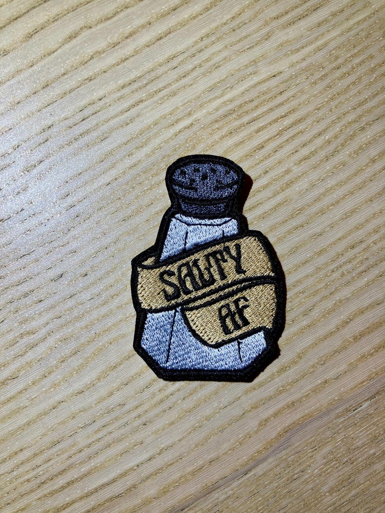 May include: A blue and white salt shaker with a black lid and a brown ribbon wrapped around it that says "SAWY AF".