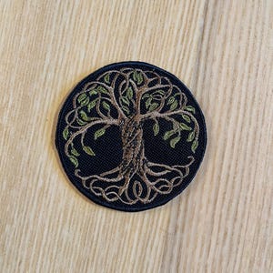 Peut inclure: Écusson brodé rond avec un motif d'arbre de vie. L'arbre est représenté avec un tronc brun et des feuilles vertes, sur un fond circulaire bleu foncé. Idéal pour les vêtements ou accessoires.