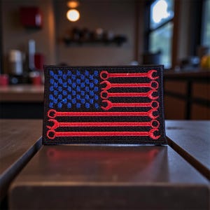 May include: Embroidered patch featuring a stylized American flag design. The flag's field of blue is filled with blue dots, and the red stripes are replaced with red wrench illustrations. The patch is on a black background.