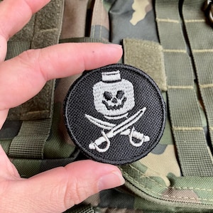 Könnte beinhalten: Schwarzer gestickter Patch mit einem weißen Totenkopf- und Knochenkreuz-Design. Der Schädel trägt eine weiße Kappe. Der Patch ist rund und hat einen schwarzen Rand.