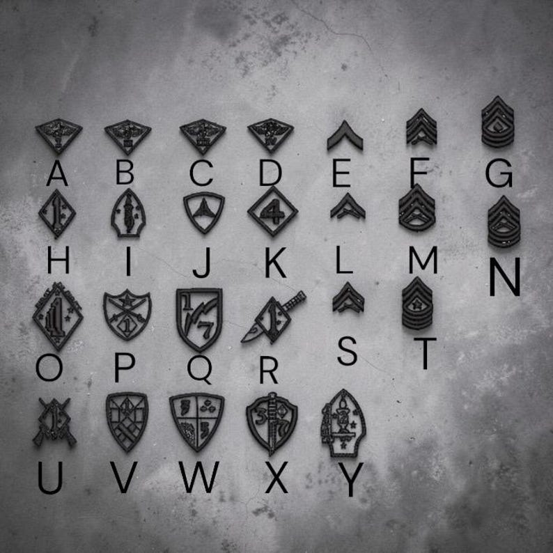 May include: A collection of black military-style patches arranged in a grid, each labeled with a letter from A to Y. The patches feature various shapes, including shields, chevrons, and diamonds, displaying symbols like numbers, swords, and stars.