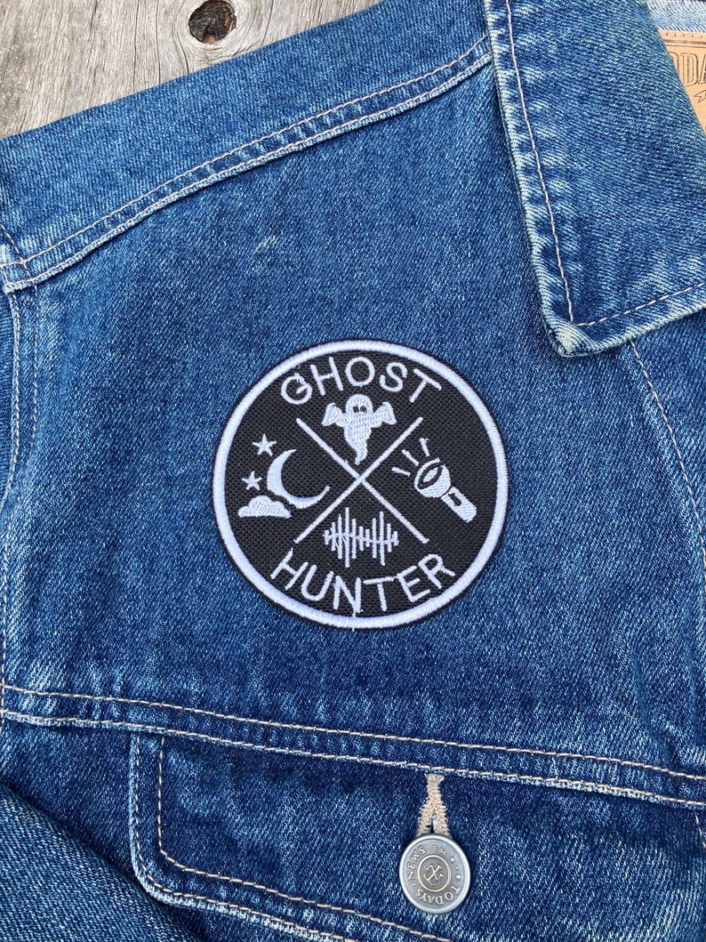 K&ouml;nnte beinhalten: Ein gestickter Patch in Schwarzwei&szlig; mit dem Text "Ghost Hunter" in einem Kreis. Der Patch zeigt ein Gespenst, einen zunehmenden Mond, eine Taschenlampe und eine Schallwelle.