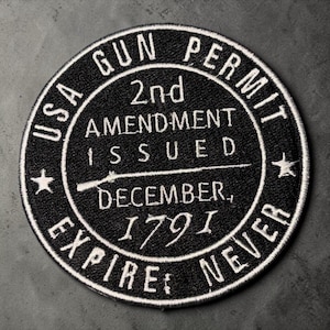 Puede incluir: Un parche circular negro bordado con costuras blancas. El texto dice USA GUN PERMIT, 2nd AMENDMENT ISSUED DECEMBER, 1791, EXPIRES: NEVER. Un gráfico de un rifle está centrado entre el texto, flanqueado por dos pequeñas estrellas blancas.