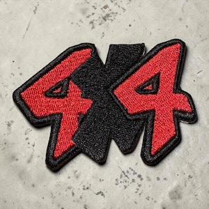 May include: Embroidered patch with the text "4x4" in red on a black background. The numbers are in a bold font and outlined in black. The patch is designed for application on clothing or accessories, possibly for a vehicle.
