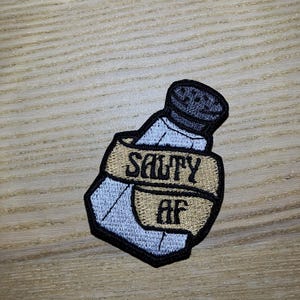 May include: A salt shaker with a gold ribbon wrapped around it that says "Salty AF".