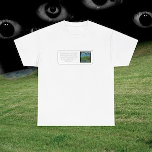 May include: White t-shirt featuring a quote about "Dreamcore" and a small image of a landscape with a boat. The quote reads: "Dreamcore is a surrealist aesthetic that uses media commonly associated with dreams, daydreams or nightmares."