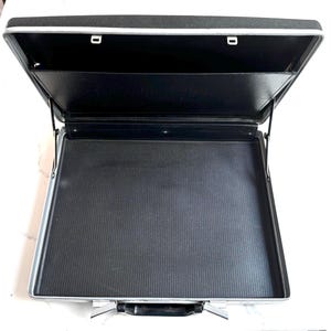 May include: A silver metal briefcase with a black interior and a black handle. The briefcase is open and the interior is visible.