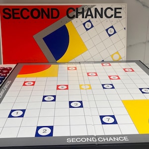 May include: A board game titled "SECOND CHANCE" with a red, white, blue, and yellow color scheme. The game board features a grid with numbered squares and colored spaces. Includes a box and game pieces.