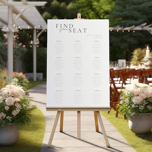Pode incluir: Um cartão de lugar de casamento branco em um cavalete com o texto "Find your seat" no topo. O cartão lista os nomes dos convidados por número de mesa.