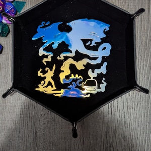 Könnte beinhalten: Schwarzes, sechseckiges Würfeltablett mit Fantasy-Motiv. Das Bild zeigt eine blau-goldene Drachenillustration, eine Figur mit einem Schwert und eine Zaubertrankflasche. Verschiedene vielseitige Würfel in verschiedenen Farben sind um das Tablett herum verstreut.