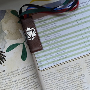 Puede incluir: Un primer plano de un libro abierto en una página sobre la clase Druida en Dungeons and Dragons. La página presenta una tabla con características de clase y una imagen de un druide con un pájaro.