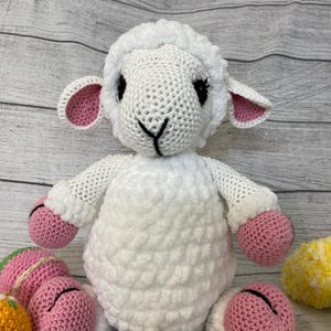 May include: A white crocheted lamb with pink ears and hooves, sitting among colorful crocheted Easter eggs.