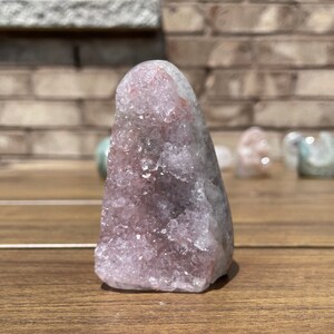 Puede incluir: Un cúmulo de cristales rosa y blanco en forma de punta. El cristal tiene una superficie rugosa y texturizada.