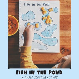 May include: A spiral-bound notebook with the title "Fish in the Pond" features blue pond shapes with numbers. Goldfish crackers are placed on the page. A child's hand is placing a cracker. A yellow bowl of crackers is on the left.