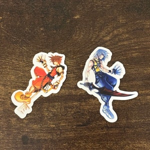 May include: Two colorful stickers featuring characters from a popular video game. The sticker on the left features a character with orange hair, a red and yellow outfit, and a keyblade. The sticker on the right features a character with blue hair, a blue and yellow outfit, and a sword.