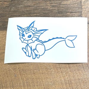 May include: A blue vinyl sticker featuring a stylized cartoon creature with fin-like ears, a frilled neck, and a long, fish-like tail. The creature is depicted in a sitting position on a white rectangular background.