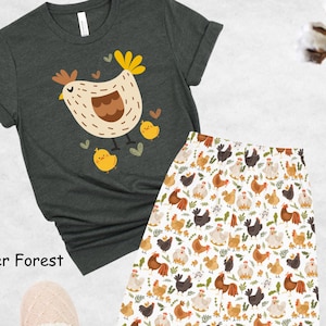 May include: A heather forest green t-shirt with a cartoon illustration of a brown hen and chicks. The t-shirt is paired with white pajama pants featuring a repeating pattern of brown, white, and black chickens.