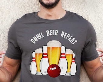 May include: A dark grey t-shirt with the text "BOWL BEER REPEAT" printed on the front. The design features a bowling ball and five bowling pins, with the middle pin replaced by a beer glass.