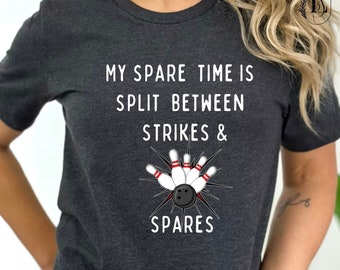 May include: Dark gray heather t-shirt with white text that reads "My spare time is split between strikes & spares". A bowling ball and pins are depicted in the center of the shirt.