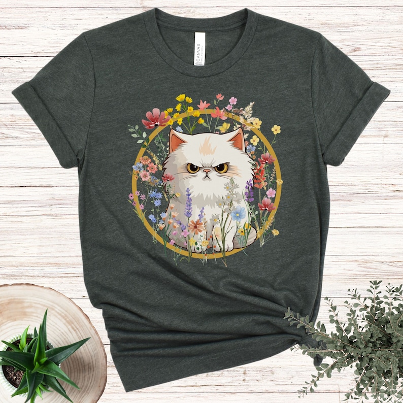 May include: A dark green t-shirt with a white cat surrounded by colorful flowers in a gold circle. The cat has a grumpy expression.