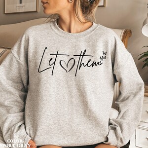May include: A gray sweatshirt with the text "Let &hearts; them" in black script with a heart and four black butterflies.