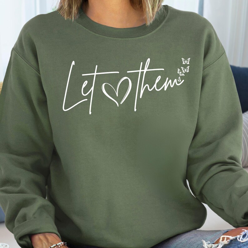 May include: A green sweatshirt with the text "Let them" in white lettering with a heart in the middle of the text. There are four small white butterflies above the text.