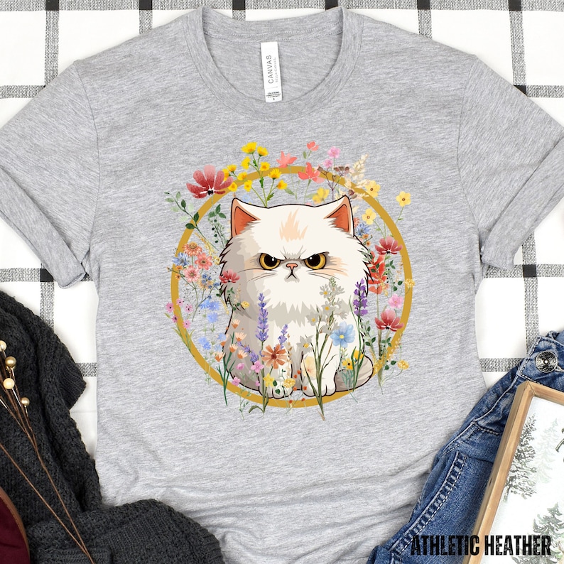 May include: A white fluffy cat with angry eyes sits in a circle of colorful flowers. The cat is surrounded by a gold circle.