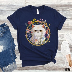 May include: A navy blue t-shirt with a white cat surrounded by colorful flowers in a gold circle. The cat has an angry expression.